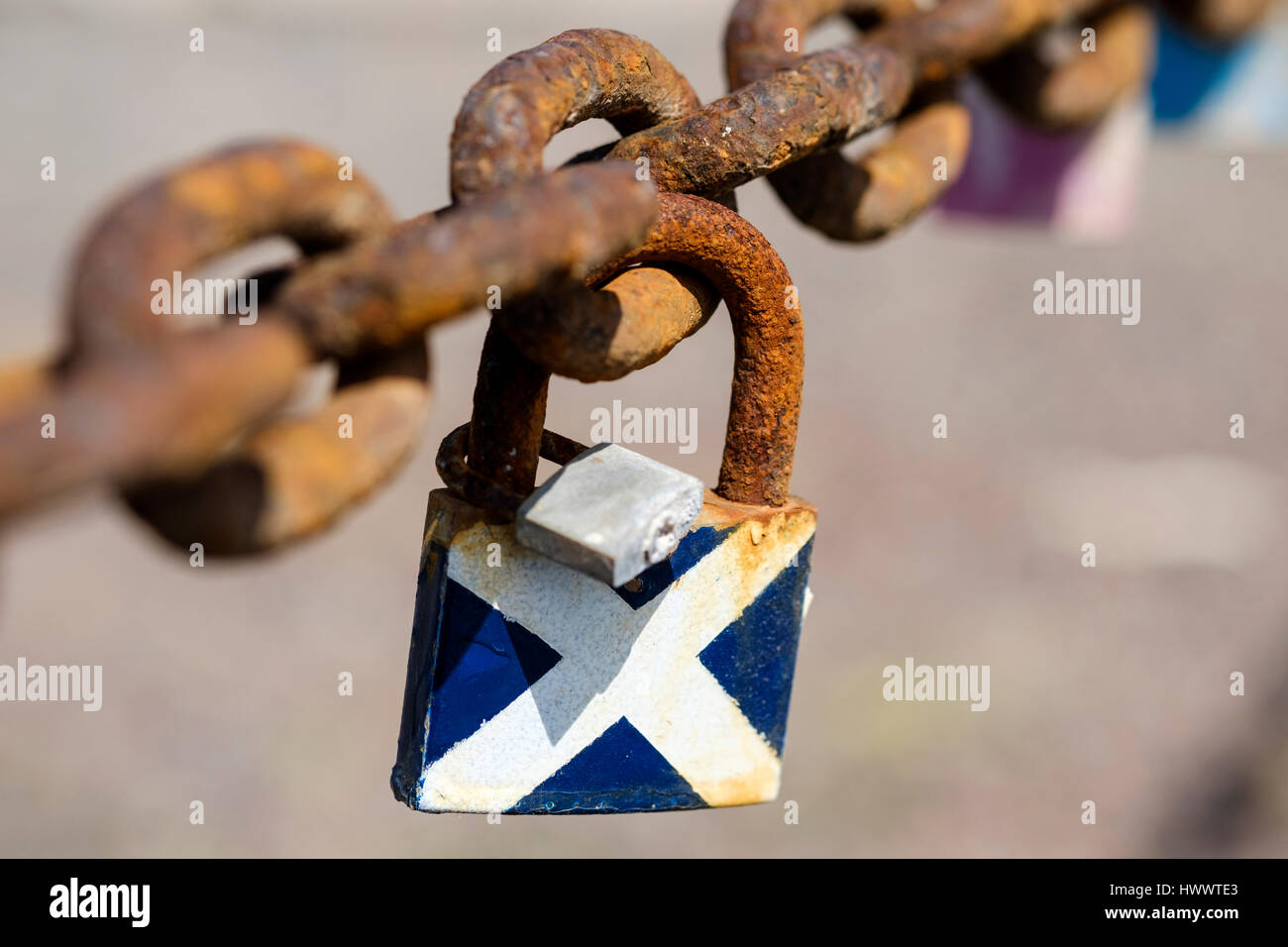 A padlock lovelock attached to an old barrier chain and painted in the colours of the Scottish Flag or st Andrews cross Stock Photo