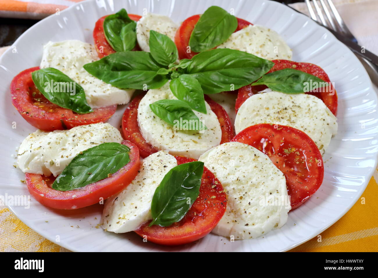 Tomato and buffalo mozzarella Caprese summer salad close up with fork in background and fresh basil on top - Italian food recipe served in white dish Stock Photo