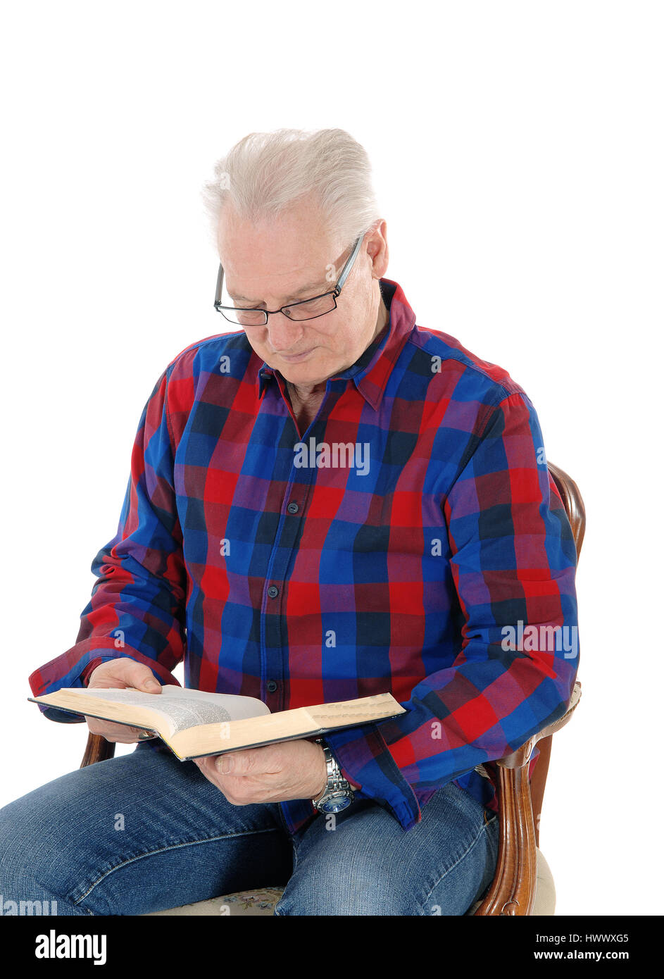 A white hair senior citizen sitting in an old armchair with his glasses and studding his bible, isolated for white background. Stock Photo