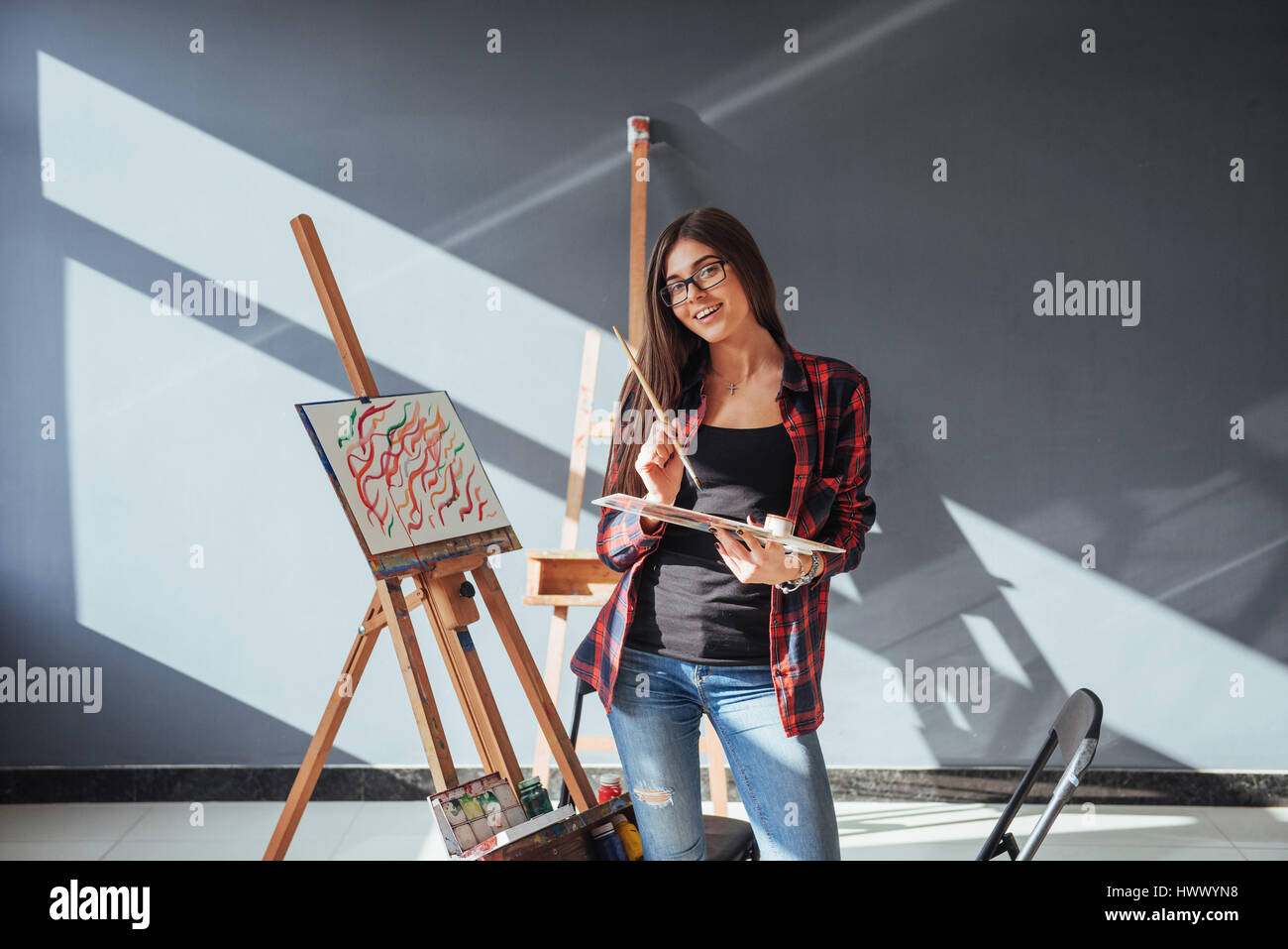Pretty Pretty Girl artist paints on canvas painting on the easel. The sun's rays breaking through window. Stock Photo