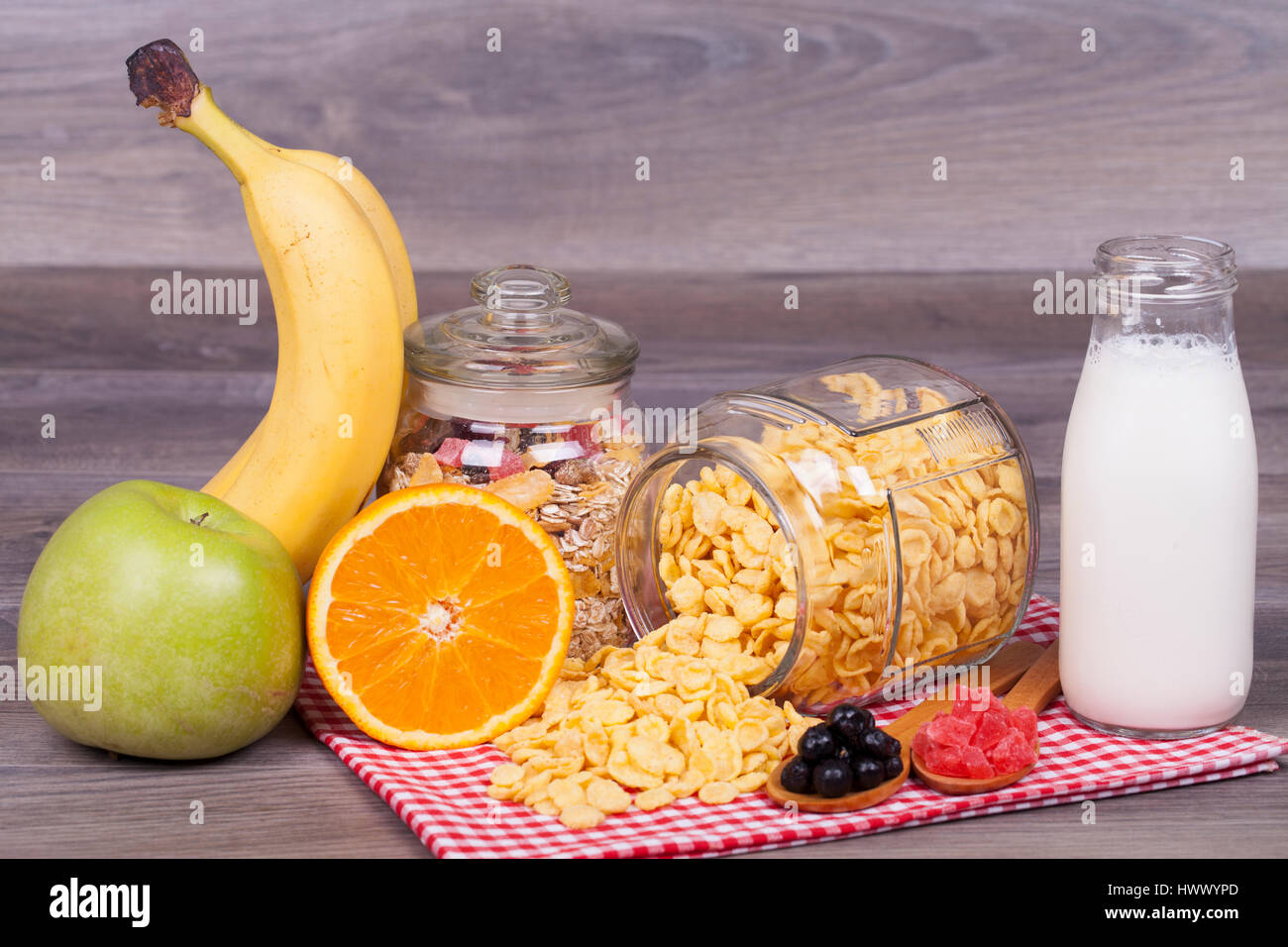 Corn flakes, muesli, orange, banana, apple, yogurt and candied fruit on a wooden background