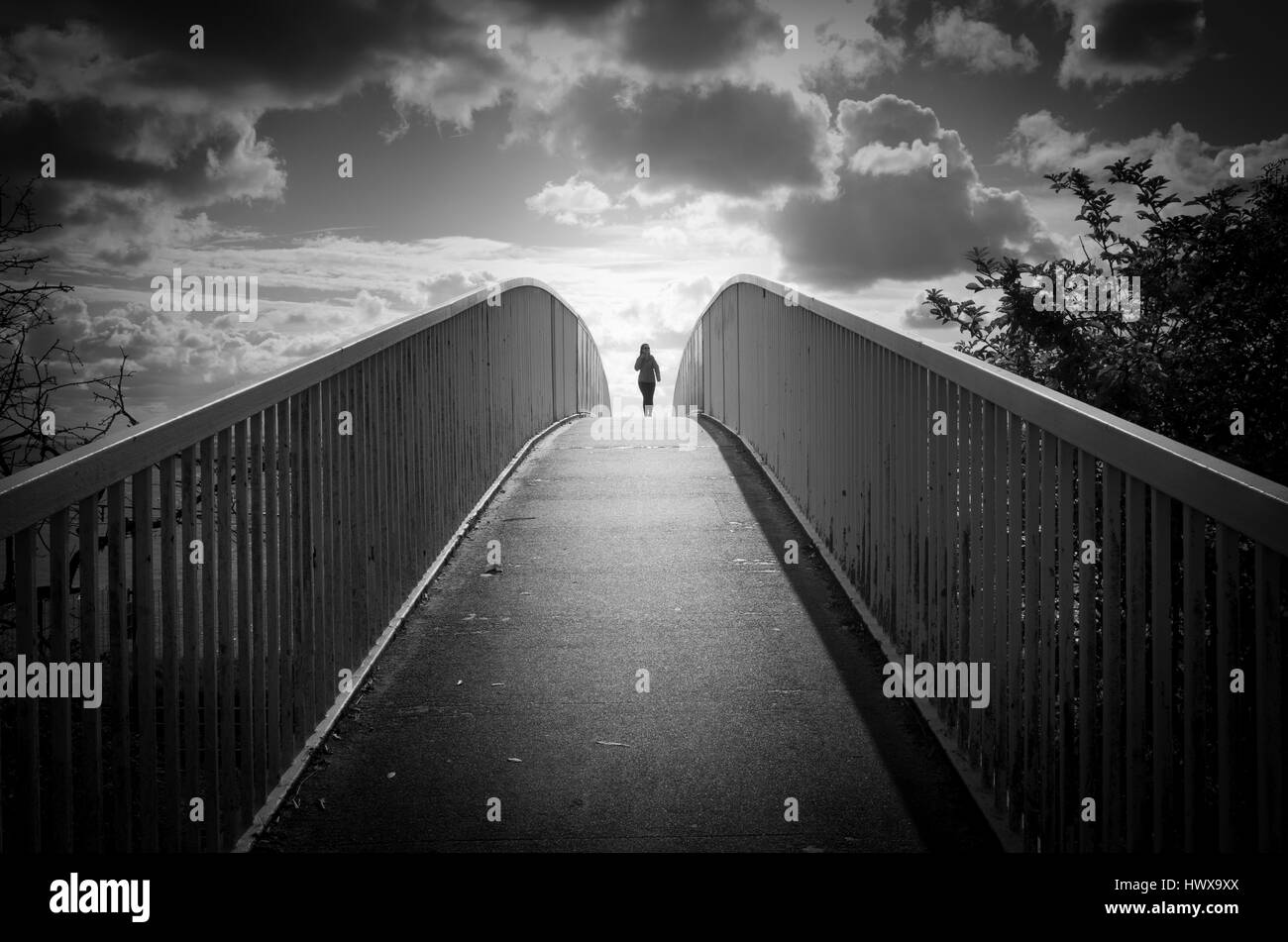 Person walking over footbridge on sunny bright day in black and white Stock Photo