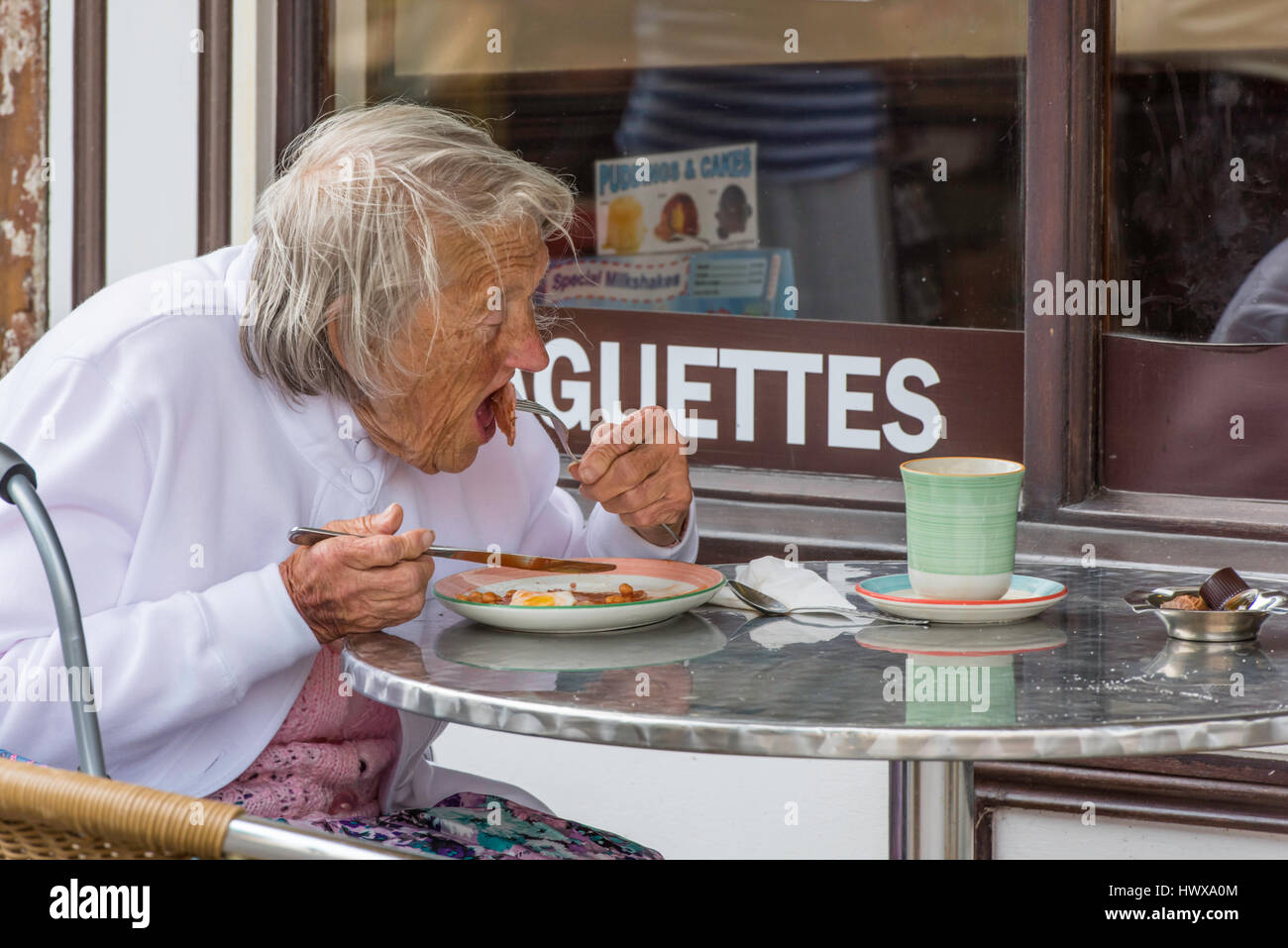 A senior woman tucking into her full English breakfast as she sits outside a cafeteria in Herne Bay town centre. Stock Photo