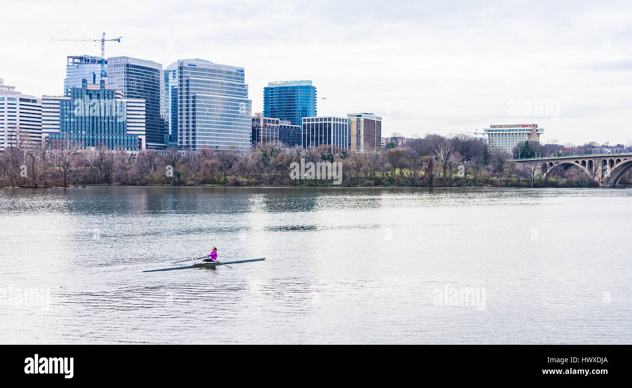 Washington DC, USA - March 20, 2017: Woman rowing on boat on Potomac river with skyline or cityscape of Arlington in Virginia Stock Photo