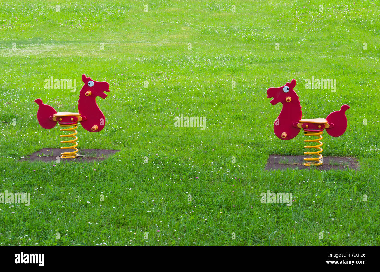 two spring horse toy surrounded by grass in the meadow of playground