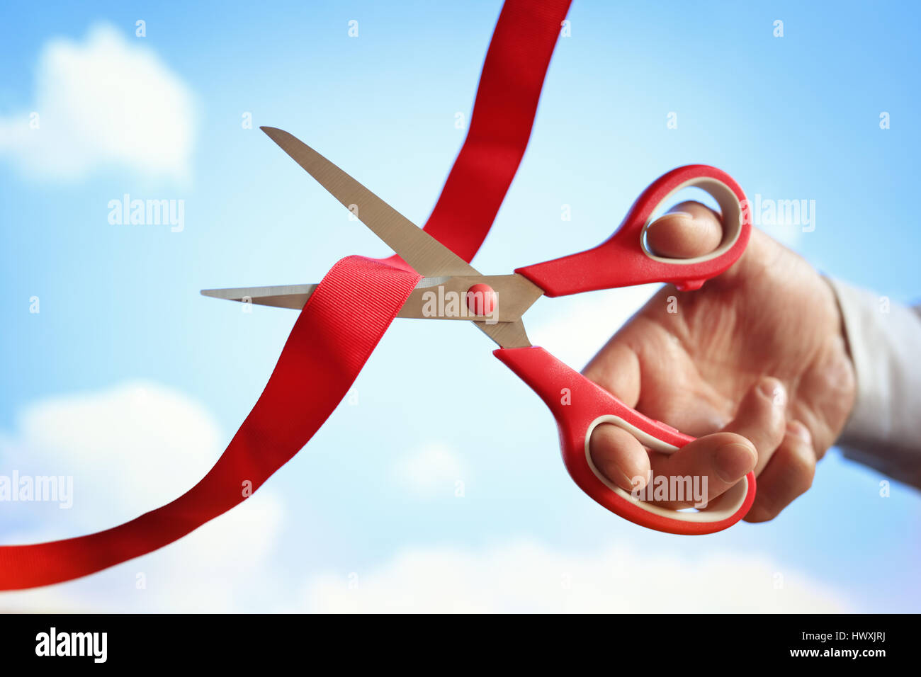 Businessman cutting a red ribbon with a pair of scissors at opening ceremony Stock Photo