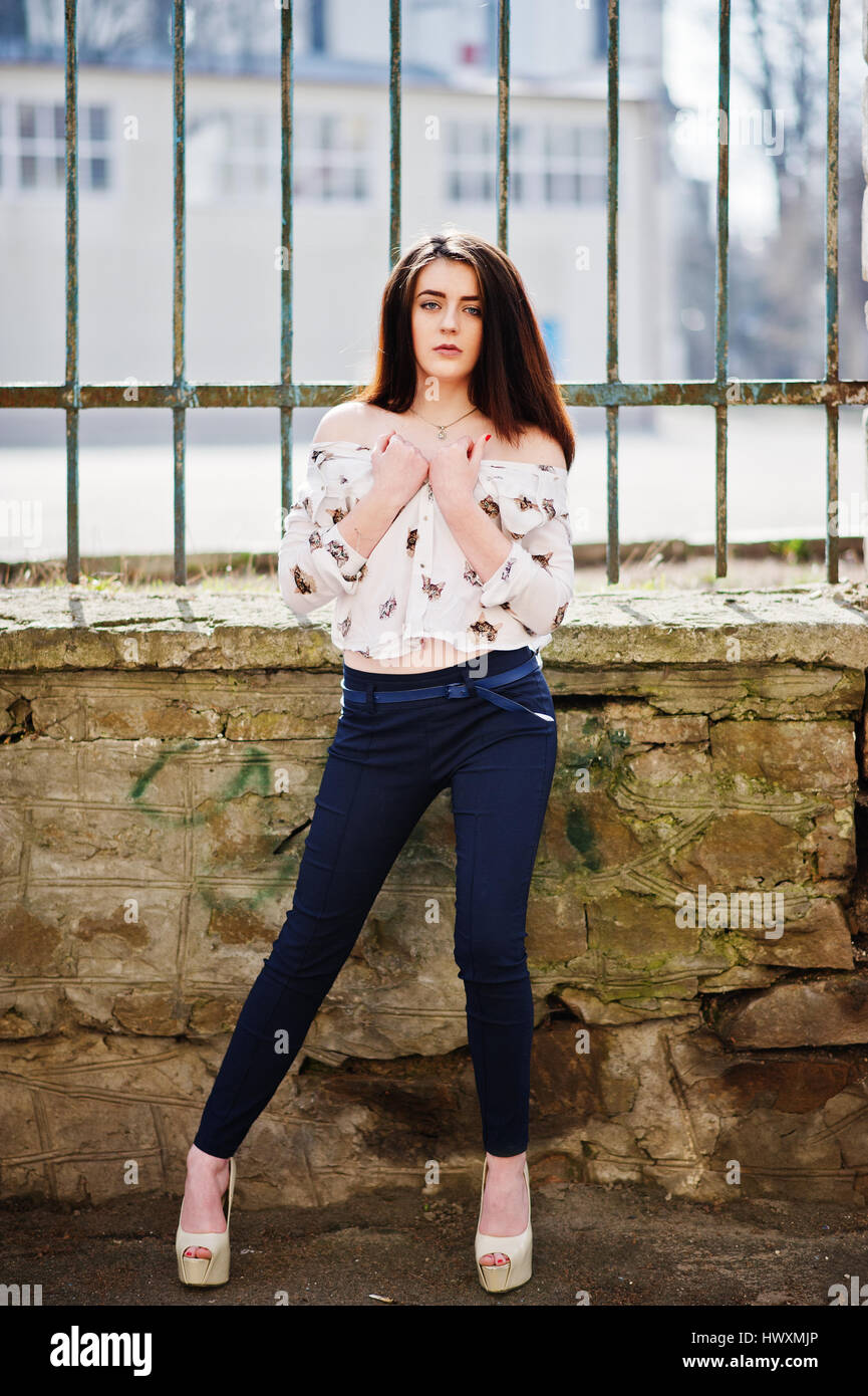 Young stylish brunette girl on shirt, pants and high heels shoes, posed  background iron fence. Street fashion model concept Stock Photo - Alamy