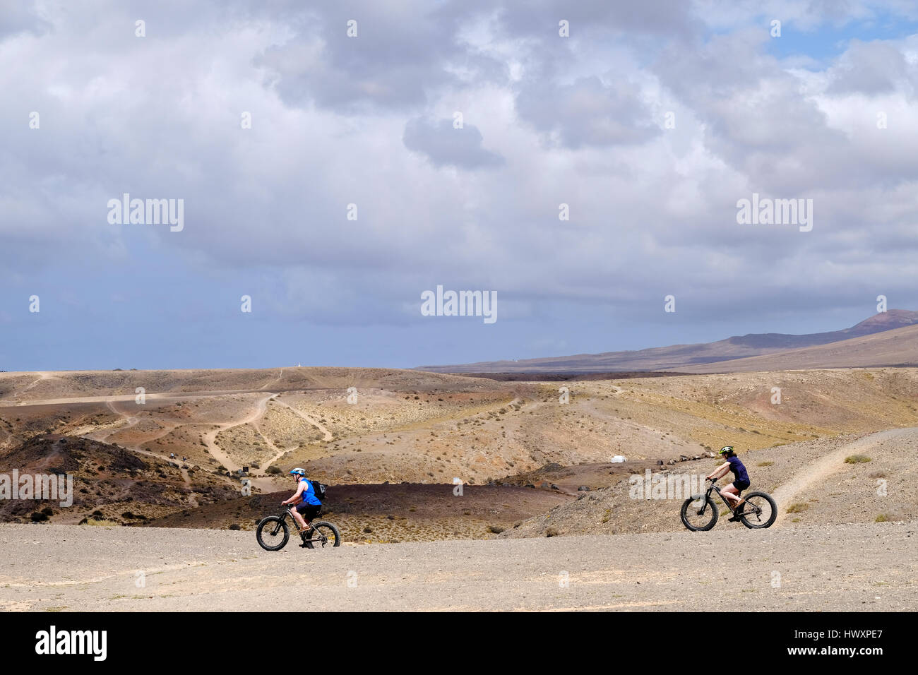 A couple, man and woman, cycle across the barren ground above Papagayo beach in lanzarote on mountain bikes adapted for the rough and rugged terrain Stock Photo