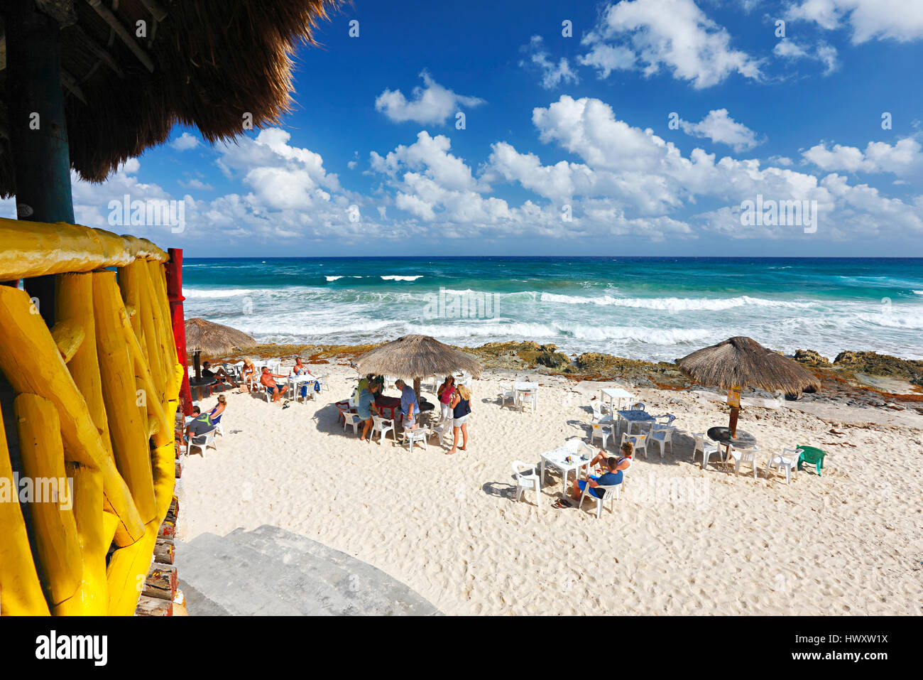 Sunny day with cloudy sky on sand beach with straw umbrellas and tourists on Cozumel Stock Photo