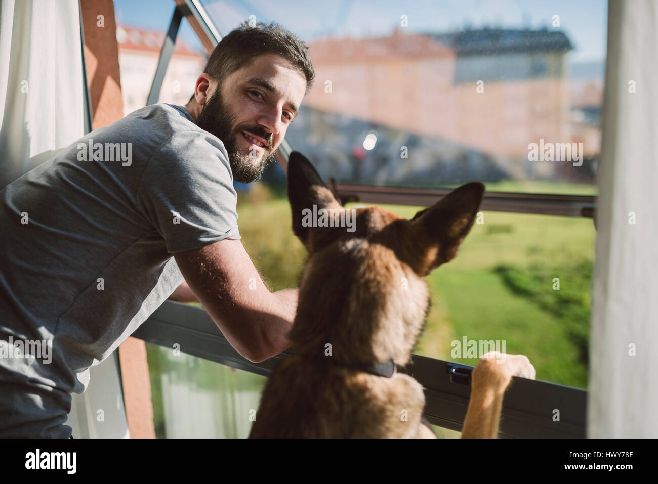 Young man standing at window with his dog, waiting Stock Photo