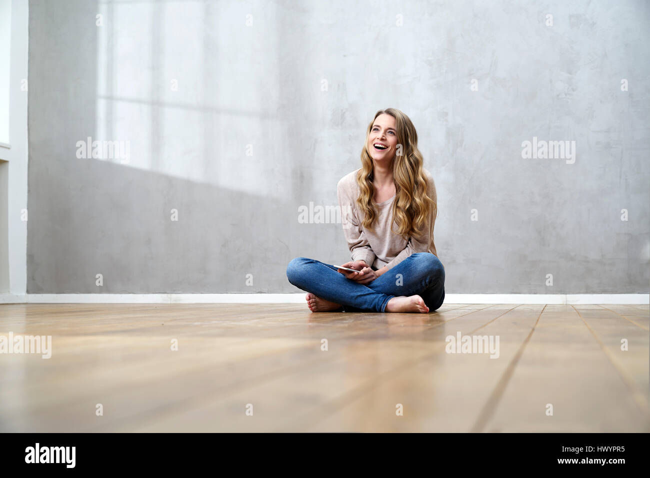 Laughing blond woman sitting on the floor with cell phone Stock Photo ...