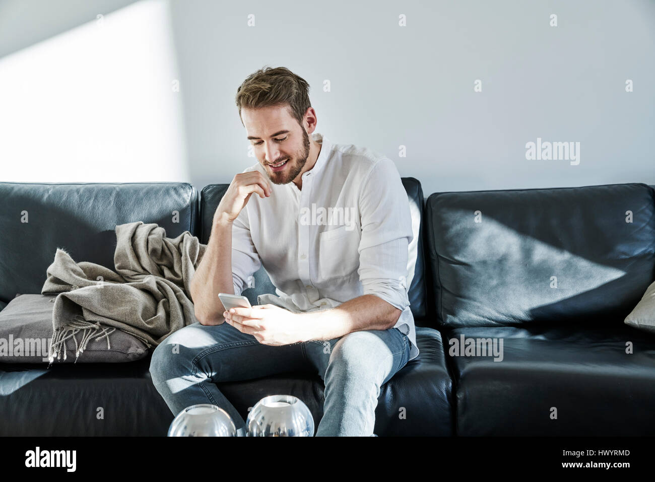 Smiling man sitting on couch looking at cell phone Stock Photo