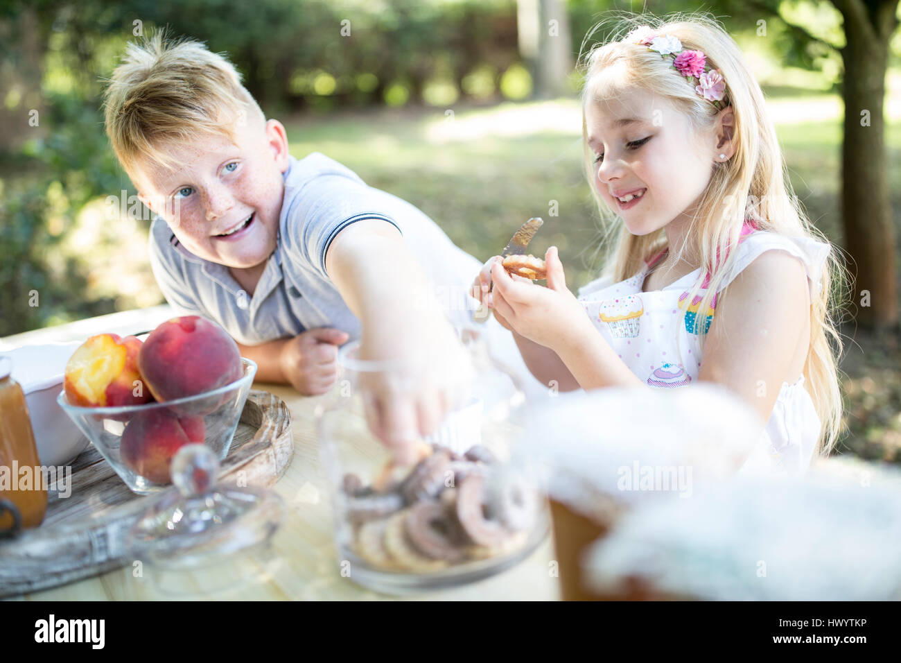 Sister and brother eating cakes at garden table Stock Photo