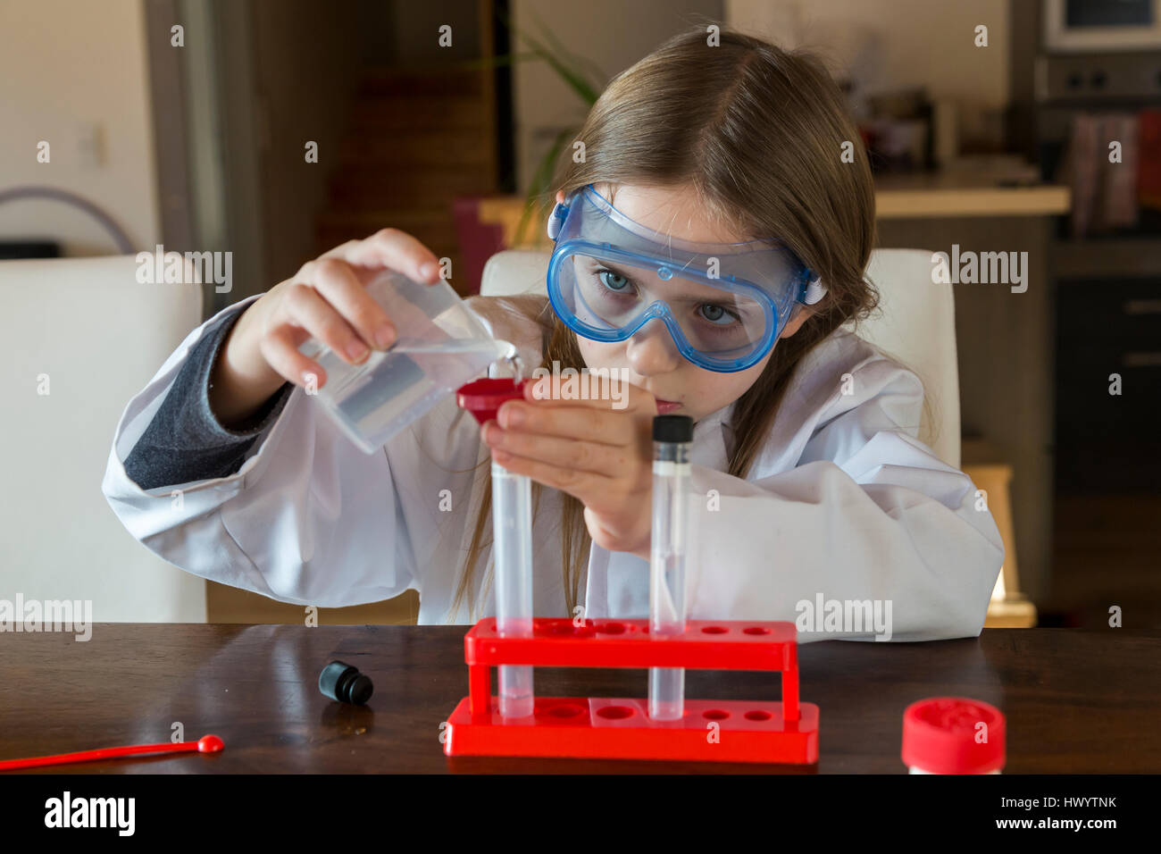 Girl wearing work coat and safety glasses using chemistry set at home Stock Photo