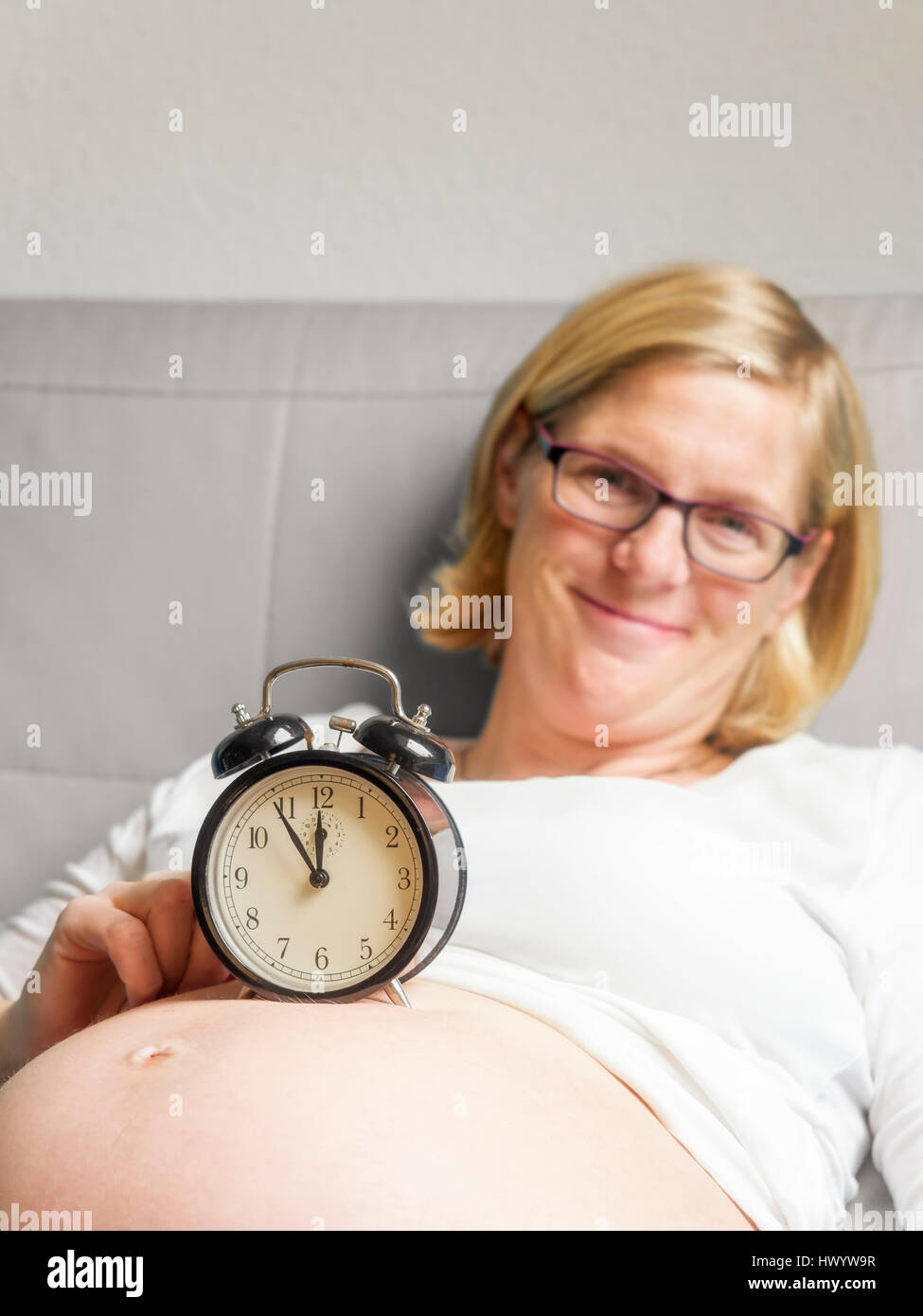 Pregnant woman with alarm clock on her belly Stock Photo