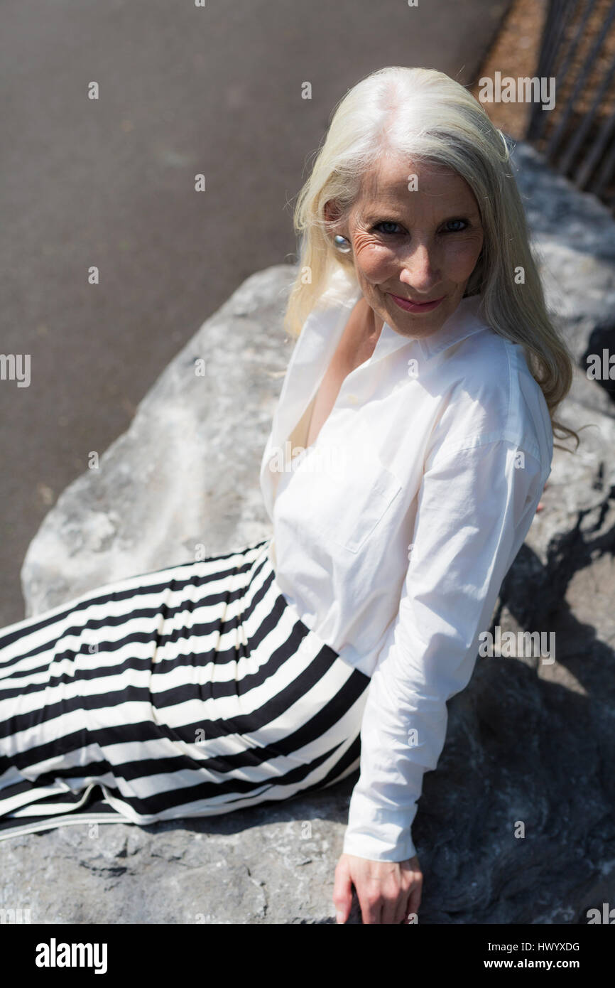 Portrait of smiling mature woman sitting on a wall looking up Stock ...