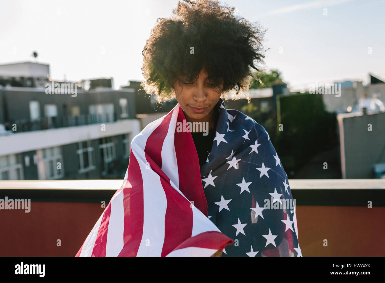Young woman standing on rooftop warpped in US American flag Stock Photo