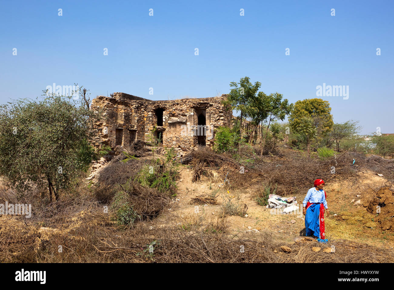 Ancient ruined buildings on a hill with a woman in traditional dress near the Jal Mahal, Narnaul, in  Rajasthan, North India under a blue sky Stock Photo