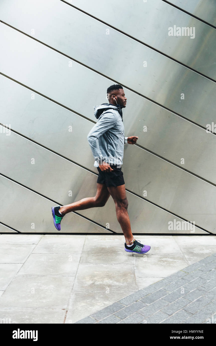 Young man running along building front Stock Photo
