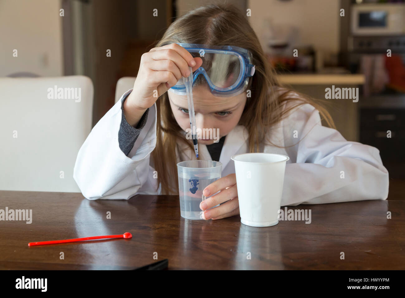 Girl wearing work coat and safety glasses using chemistry set at home Stock Photo