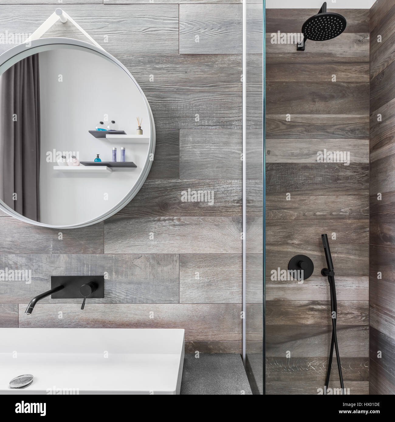 Modern bathroom with shower, round mirror and wood effect tiling Stock