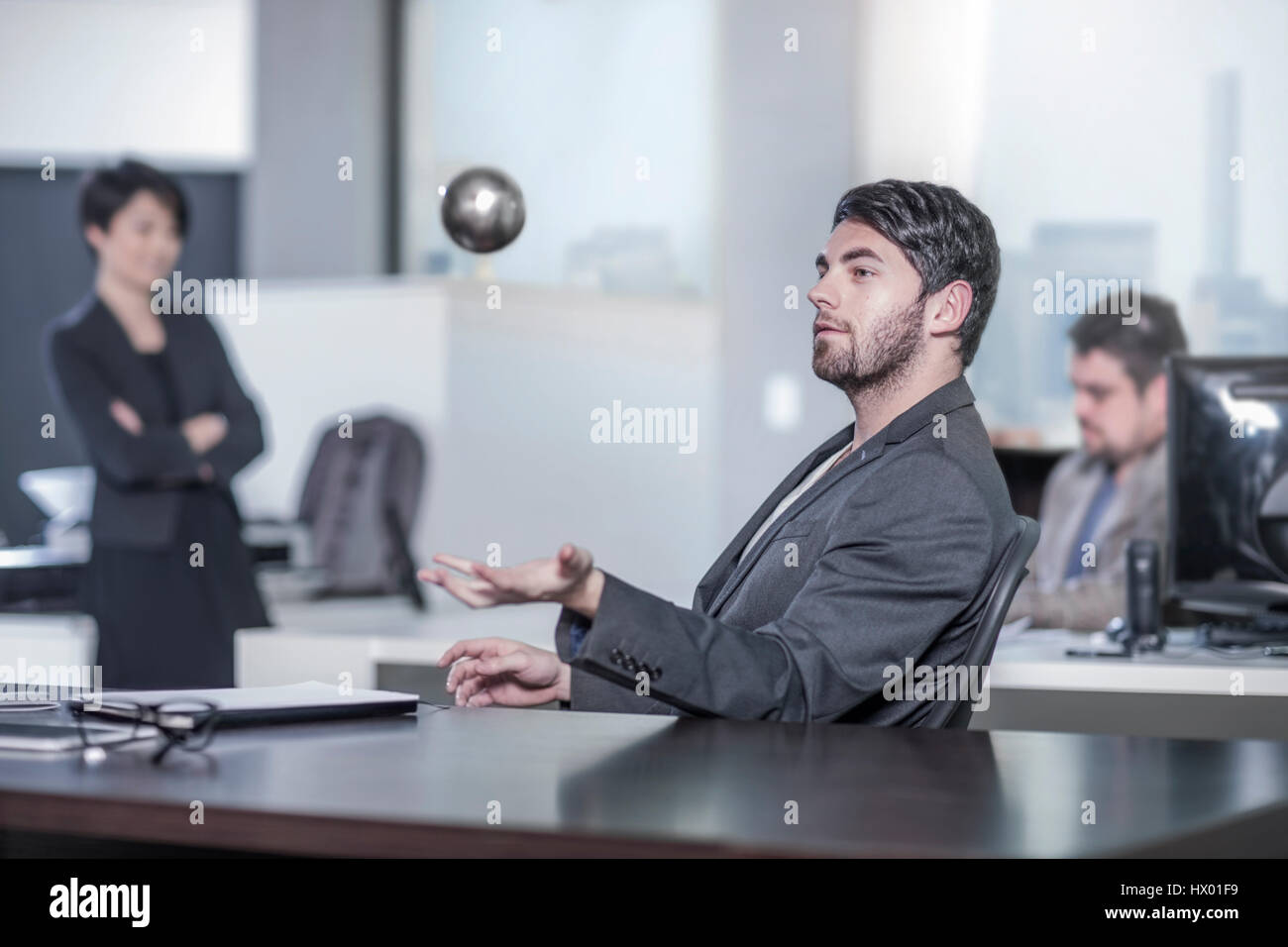 Man Sitting At Desk In City Office Throwing A Ball In The Air