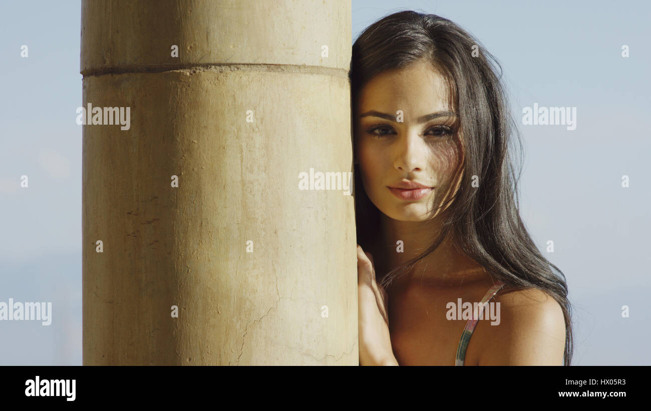 Portrait of sultry woman with long hair standing behind pole Stock Photo