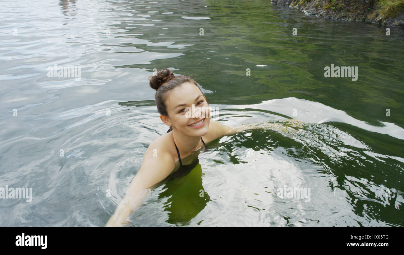 High angle portrait of smiling woman in bikini swimming in remote pool of water Stock Photo