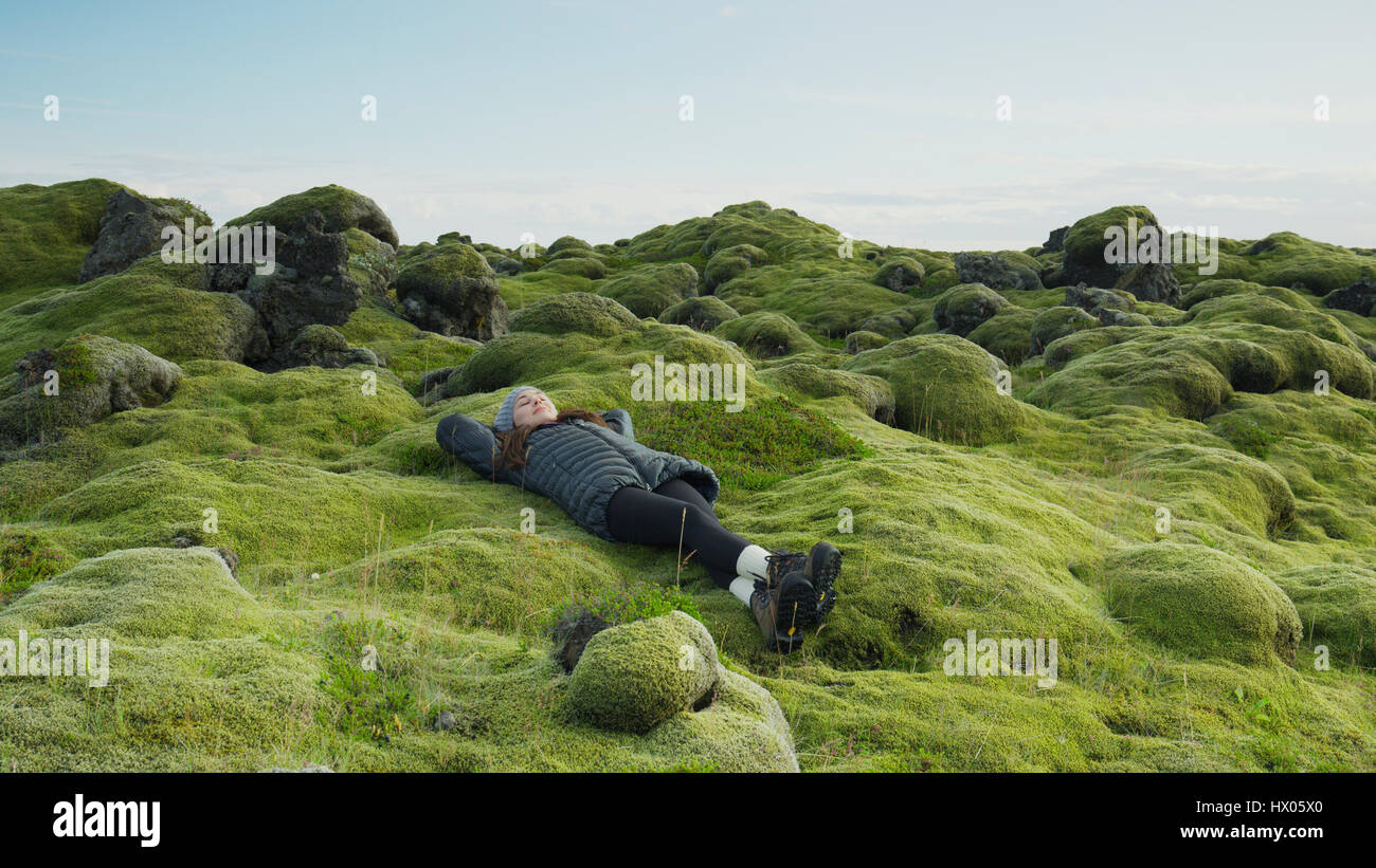 High angle view of woman laying in mossy field in remote rocky landscape under clear blue sky Stock Photo