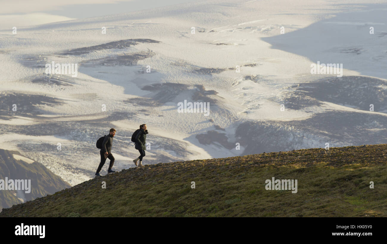 High angle view of hikers walking on grassy hilltop over snowy remote landscape Stock Photo