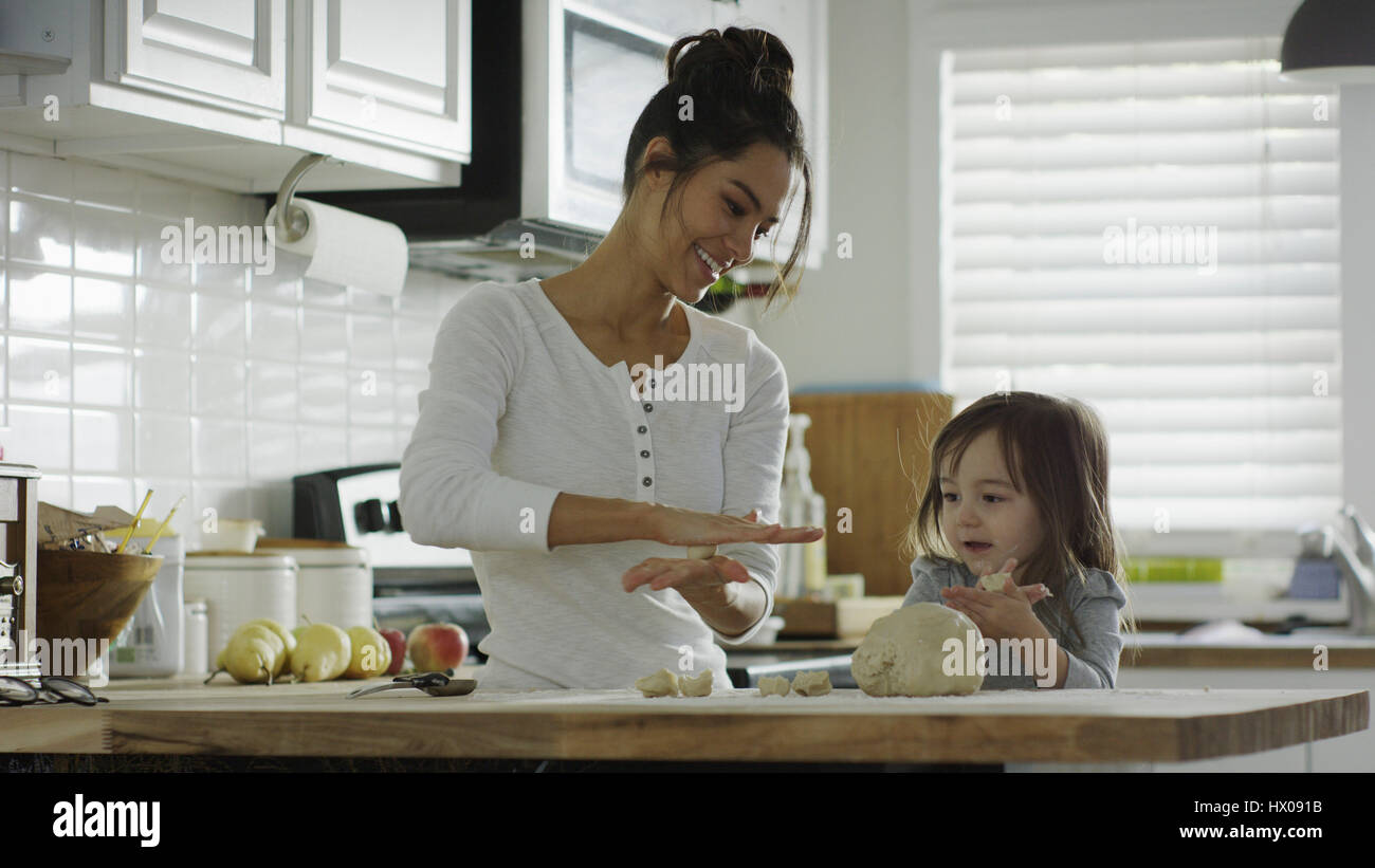 Smiling mother teaching daughter to bake and roll dough in kitchen Stock Photo