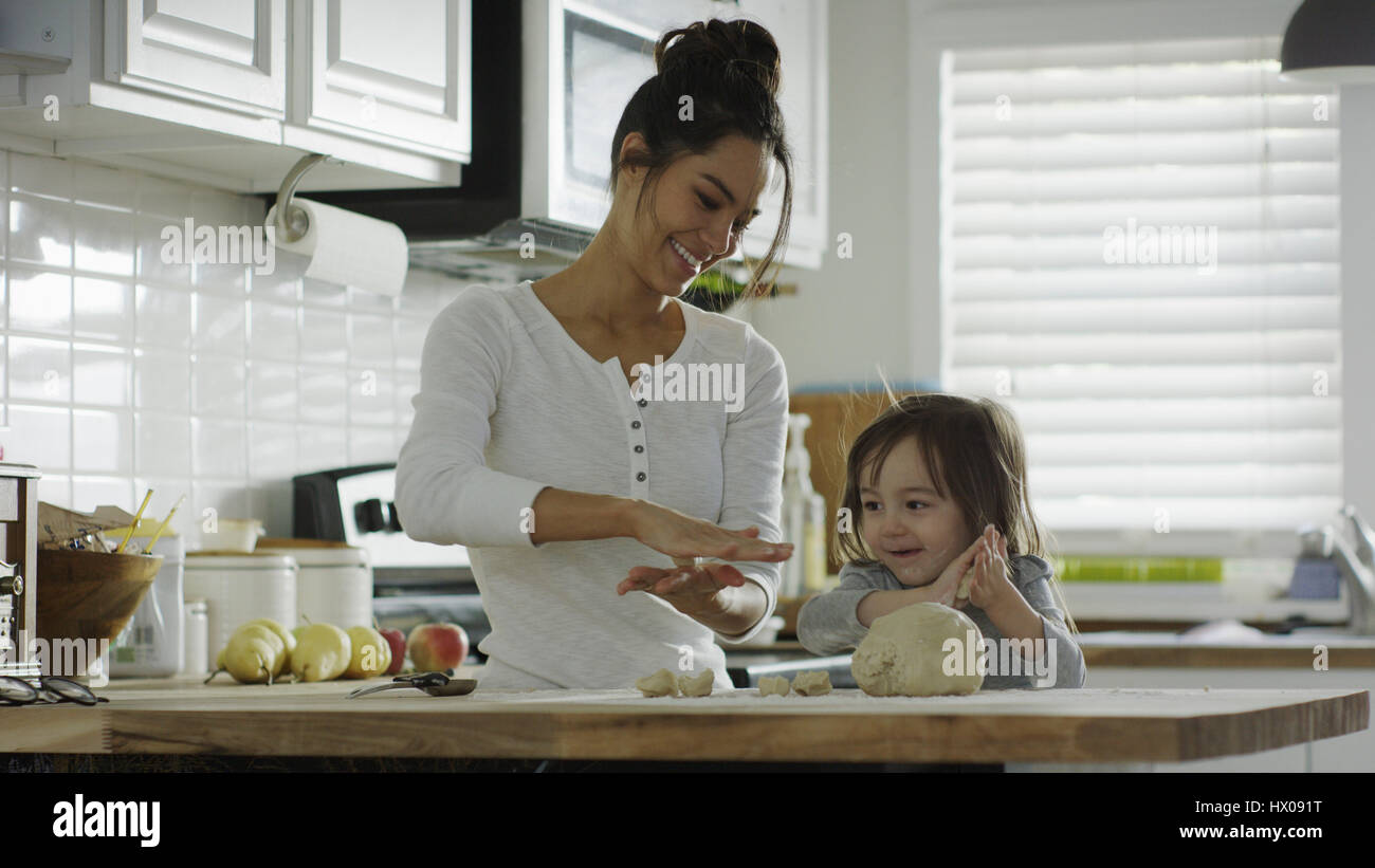 Smiling mother teaching daughter to bake and roll dough in kitchen Stock Photo