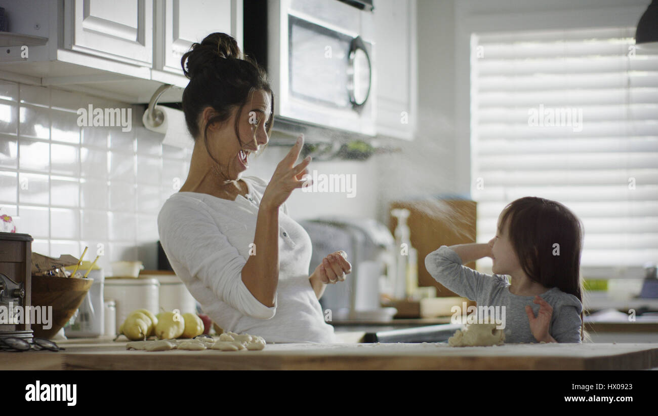 Blurred playful mother and daughter baking and tossing dough in kitchen Stock Photo