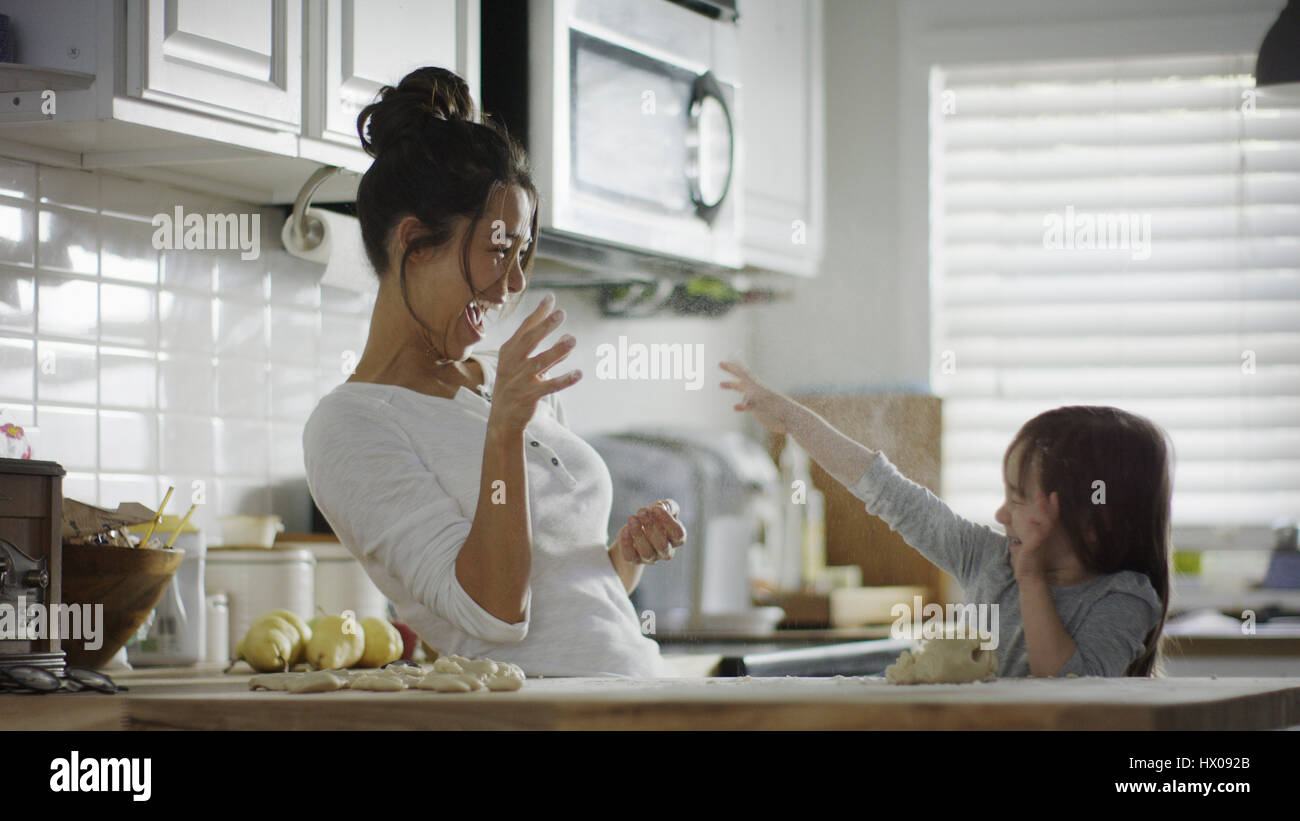 Playful mother and daughter baking and tossing dough in kitchen Stock Photo