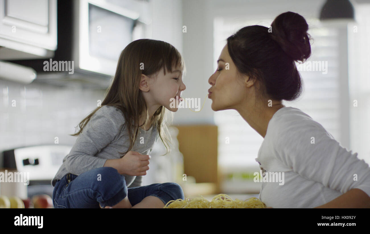 Profile of playful mother and daughter kissing over spaghetti pasta in