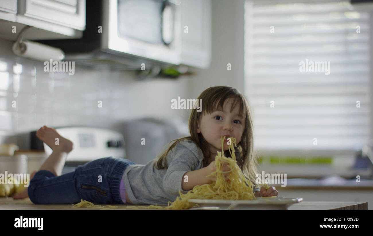 Naughty messy girl laying on kitchen counter eating plate of spaghetti Stock Photo