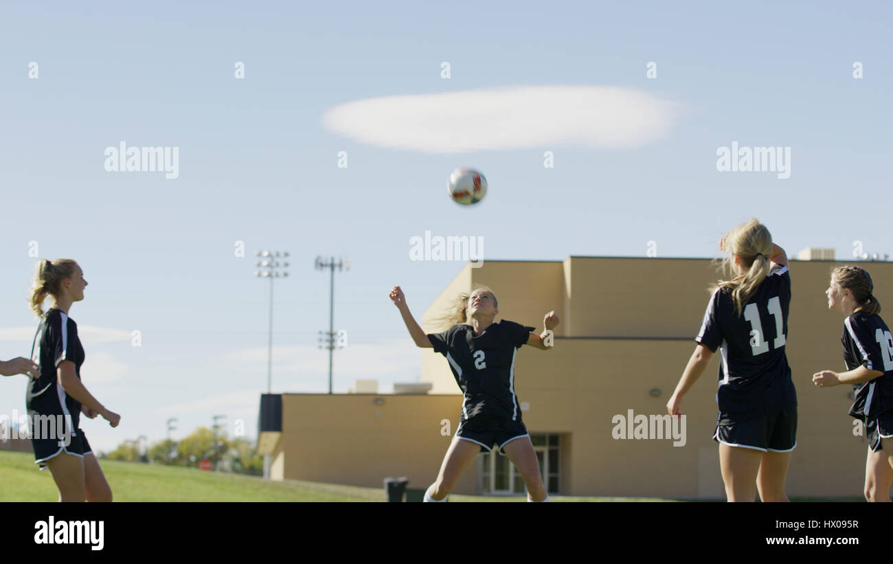 Athlete with soccer teammates hitting ball with head in soccer goal under blue sky Stock Photo