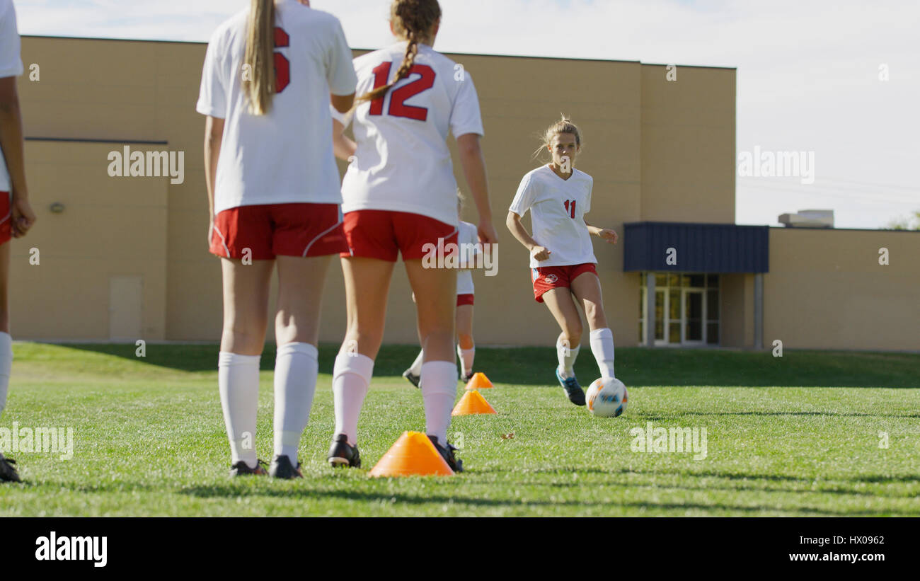 Athlete with soccer teammates kicking ball in soccer goal on field Stock Photo