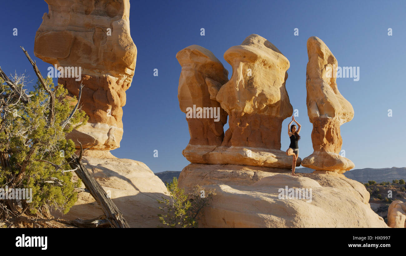 Low angle view of woman practicing yoga and meditating on rock formations in remote desert landscape under clear blue sky Stock Photo