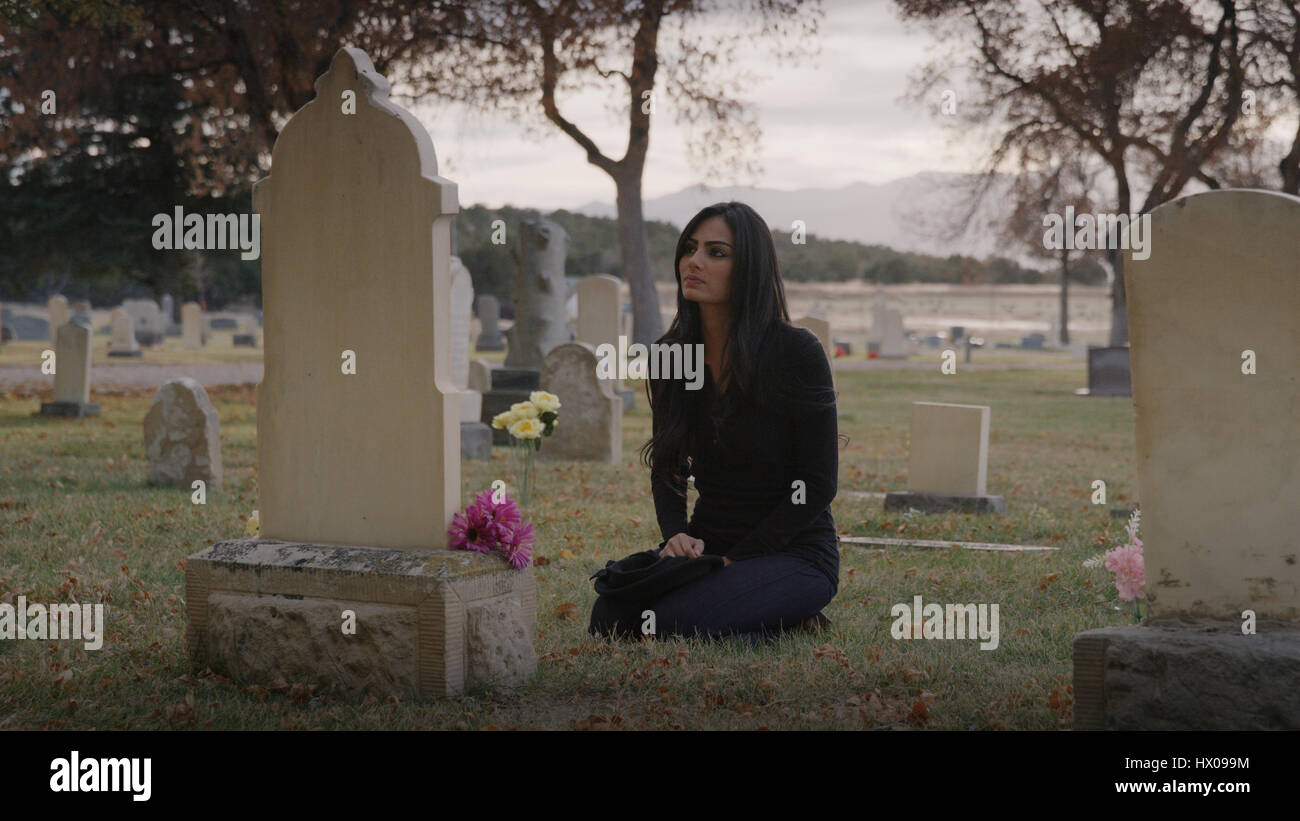 Sad pensive woman sitting at grave in lonely cemetery Stock Photo