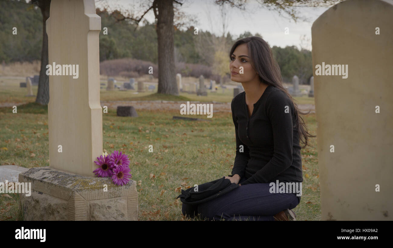Sad pensive woman sitting at grave in lonely cemetery Stock Photo
