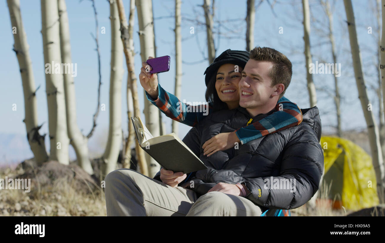 Low angle view of smiling couple hugging and posing for smartphone selfie in autumn woods Stock Photo