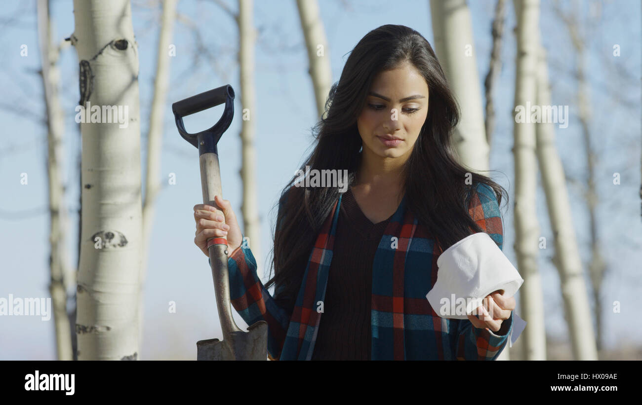 Low angle view of upset woman holding toilet paper and shovel in remote woods Stock Photo