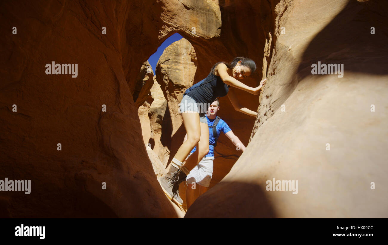 Low angle selective focus view of boyfriend and girlfriend exploring cave in scenic rock formations Stock Photo