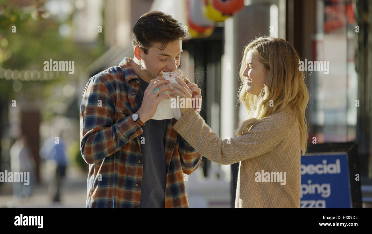 Smiling girlfriend feeding boyfriend sandwich outside store Stock Photo