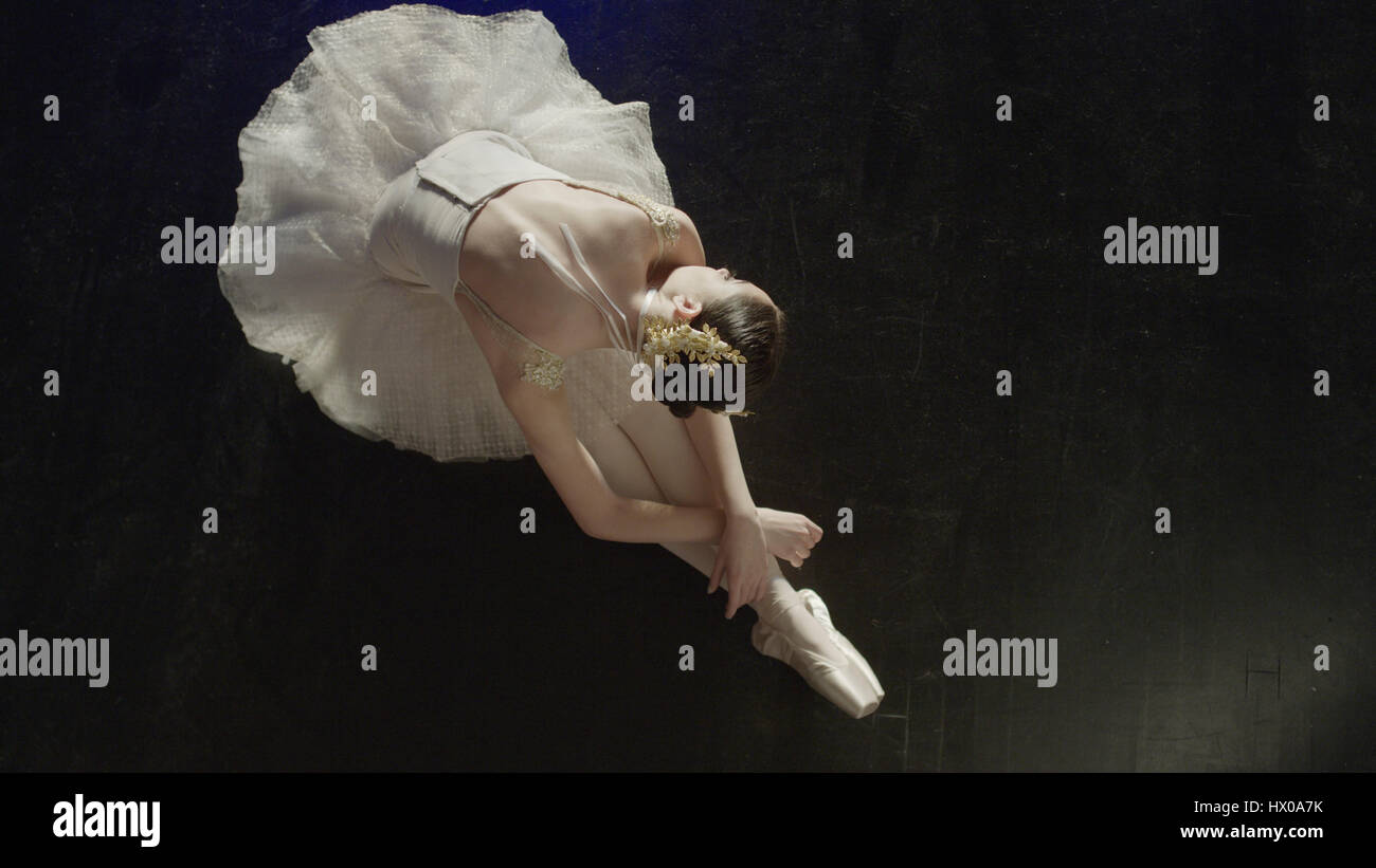 High angle view of performing dancer ballerina in tutu and toe shoes laying gracefully on stage floor Stock Photo