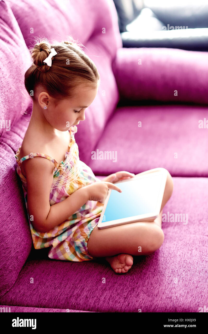 Little pretty girl with a tablet computer on a sofa at home Stock Photo ...