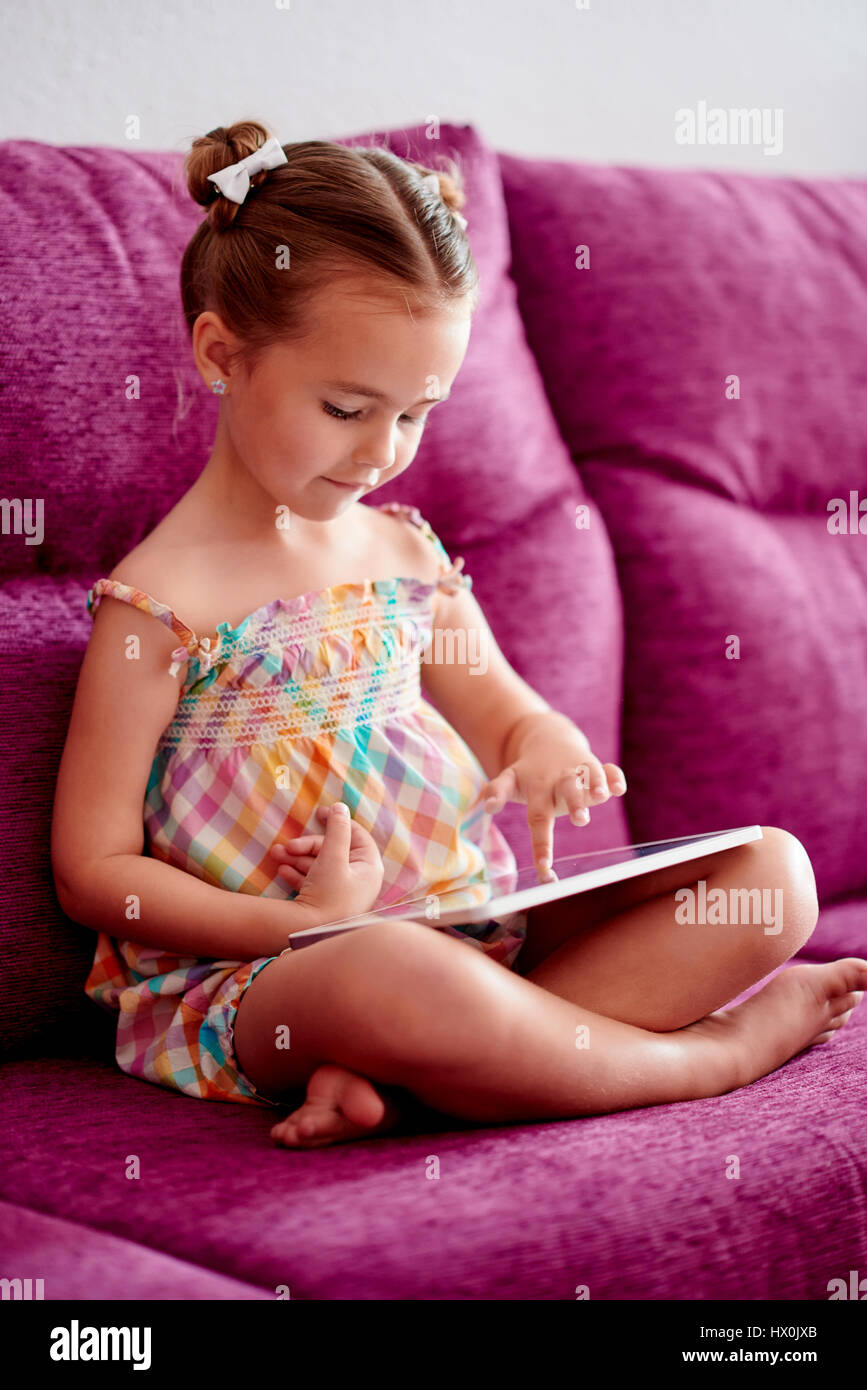 Little pretty girl with a tablet computer on a sofa at home Stock Photo ...