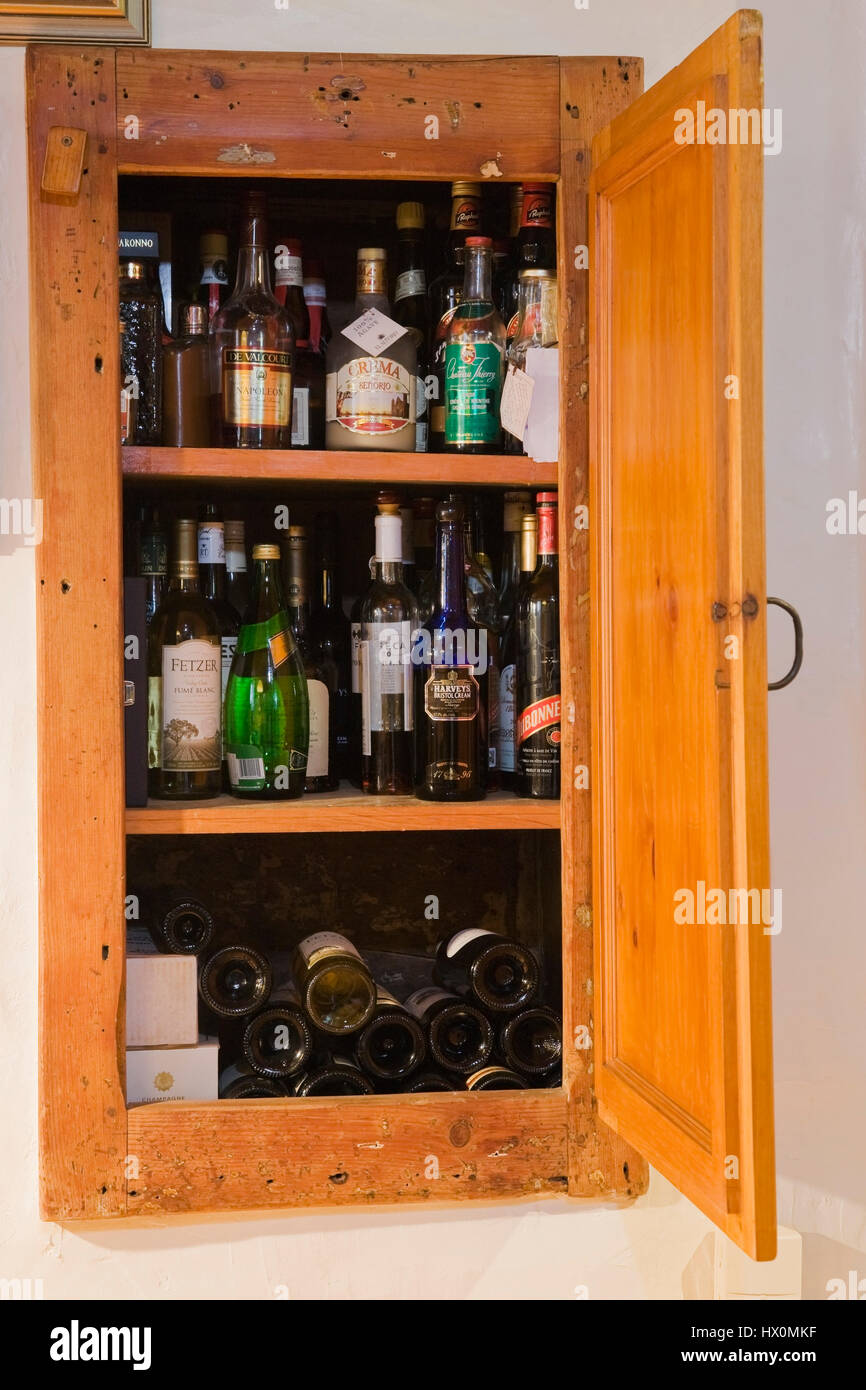 Stored liquor and wine bottles inside a recessed pantry built into exterior dining room wall of 1740 old house interior. Stock Photo