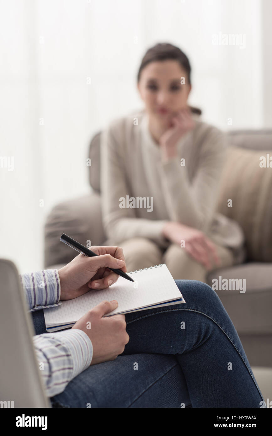 Psychologist listening to her patient and writing down notes, mental health and counseling concept Stock Photo